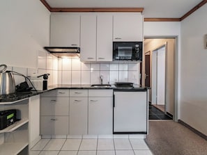 A compact kitchen with white cabinets, a microwave, a kettle, and a small refrigerator. - Paradies 012 Appartement/Fewo,  , 3-Bettwohnung 3-Bettwohnung by Interhome (Arosa)