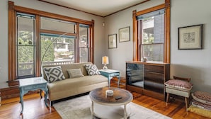 A living room with a sofa, coffee table, side table, and a television. - Historic Queen Anne Omaha Home in Field Club (Omaha)