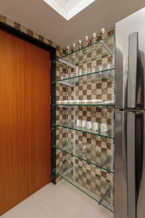 Una cocina con una estantería de vidrio que exhibe cristalería, un refrigerador de acero inoxidable y un salpicadero de azulejos con diseño.