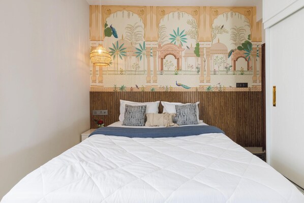 A bed with a white quilt, a wooden headboard, and a wall tapestry.