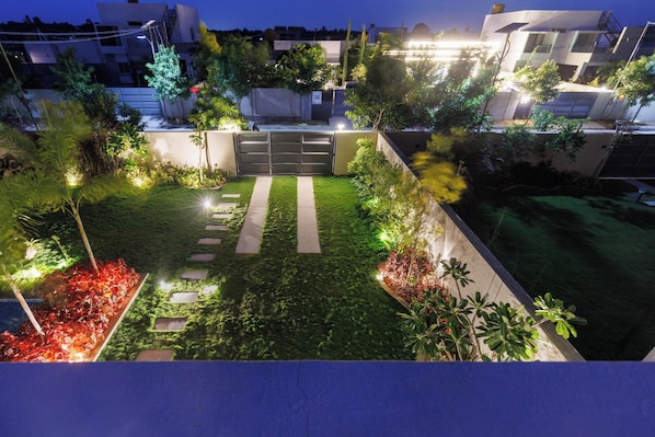 Un jardín cuidado con un camino empedrado, una entrada protegida por una reja y vegetación circundante.