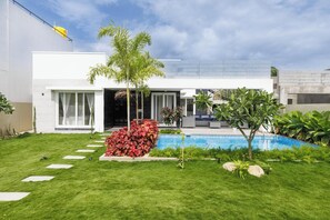 A modern house with a swimming pool, a well-maintained lawn, and a variety of plants.