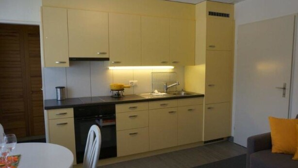 A compact kitchen with a dining area, a sofa, and a table with a candle. - Paradies 505 Appartement/Fewo,  , 2-Bettwohnung 2-Bettwohnung by Interhome (Arosa)