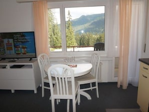 Ein Zimmer mit Esstisch und Stühlen, einem Fernseher und einem Fenster mit Bergblick.