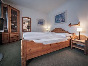 Ein hölzernes Bett mit Kopfteil, zwei Nachttische mit Lampen, ein Holzschrank und zwei gerahmte Bilder an der Wand.