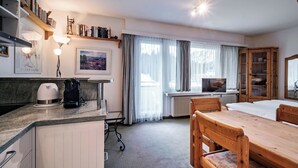 A hotel room with a dining table, chairs, a kitchen area with a coffee maker, a TV, and a large window with curtains. - Paradies 607 Appartement/Fewo,  , 2-Bettwohnung 2-Bettwohnung by Interhome (Arosa)