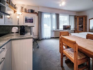 A hotel room with a dining table, chairs, a kitchen area with a coffee maker, a TV, and a large window with curtains. - Paradies 607 Appartement/Fewo,  , 2-Bettwohnung 2-Bettwohnung by Interhome (Arosa)