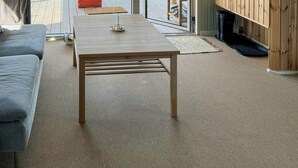 En moderne stue med sofa, bord og fjernsyn, store glasdøre til et udendørs område med et køretøj og grøntområde.