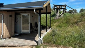 En træbygning med en overdækket veranda, en dør og et lille udendørs siddeområde.