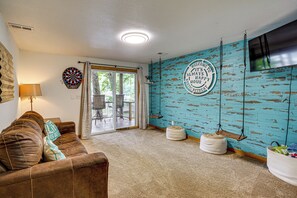 Een woonkamer met een bruine leren bank, een dartbord, een televisie en een blauwe houten wand met een bordje welkom.