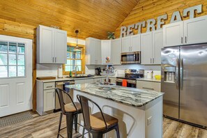 A kitchen with a central island, bar stools, a stainless steel refrigerator, and a microwave. - Osage Beach Cabin With Private Dock and Lily Pad (Osage Beach)