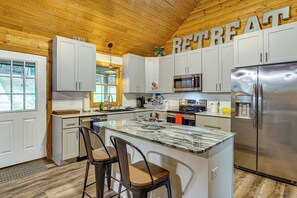 A kitchen with a central island, bar stools, a stainless steel refrigerator, and a microwave. - Osage Beach Cabin With Private Dock and Lily Pad (Osage Beach)