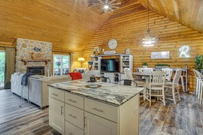 A cozy cabin interior with a stone fireplace, wooden walls, a dining area, and a kitchen with a large island. - Osage Beach Cabin With Private Dock and Lily Pad (Osage Beach)