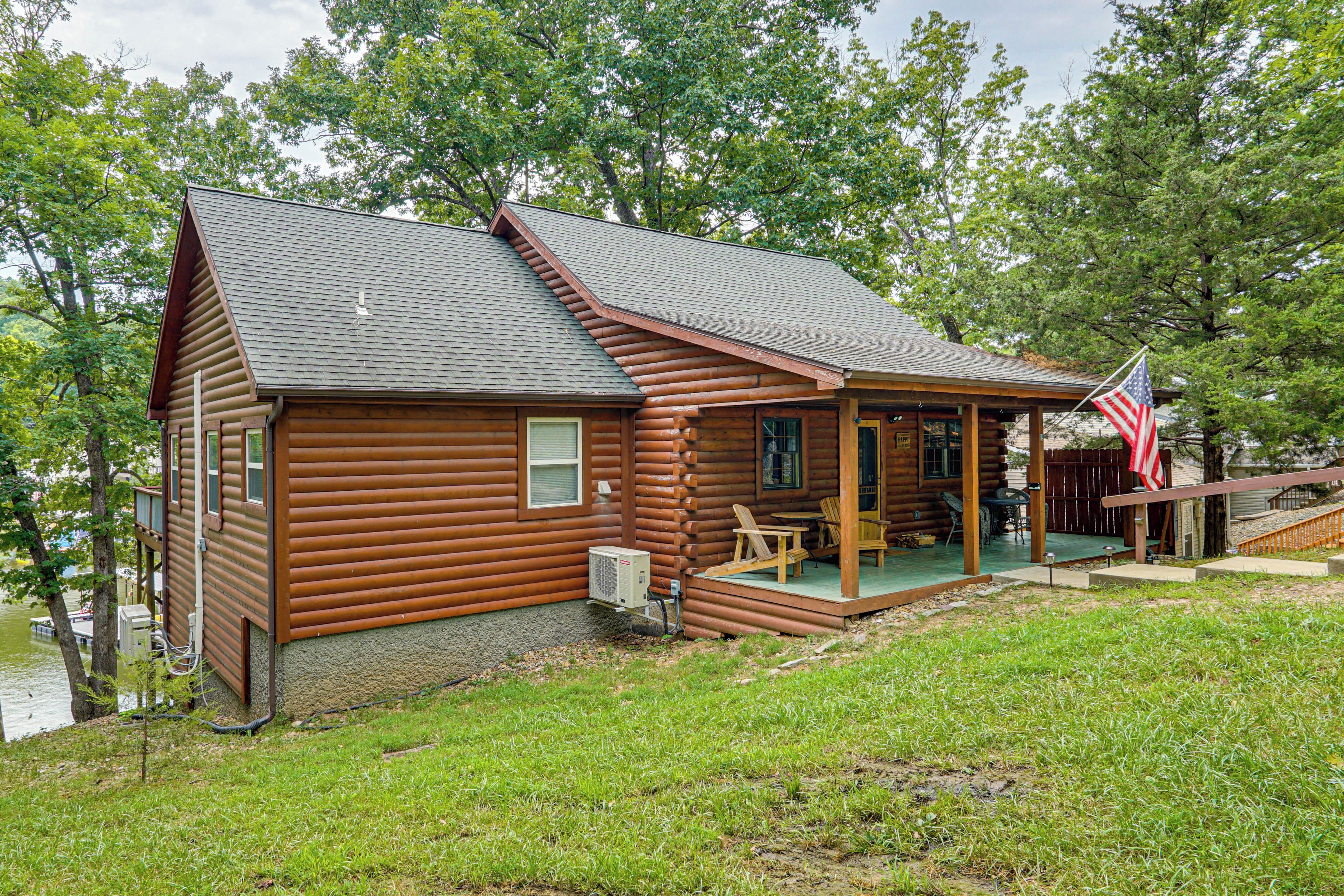 Une cabane en rondins avec un porche, des sièges d’extérieur et un drapeau américain.