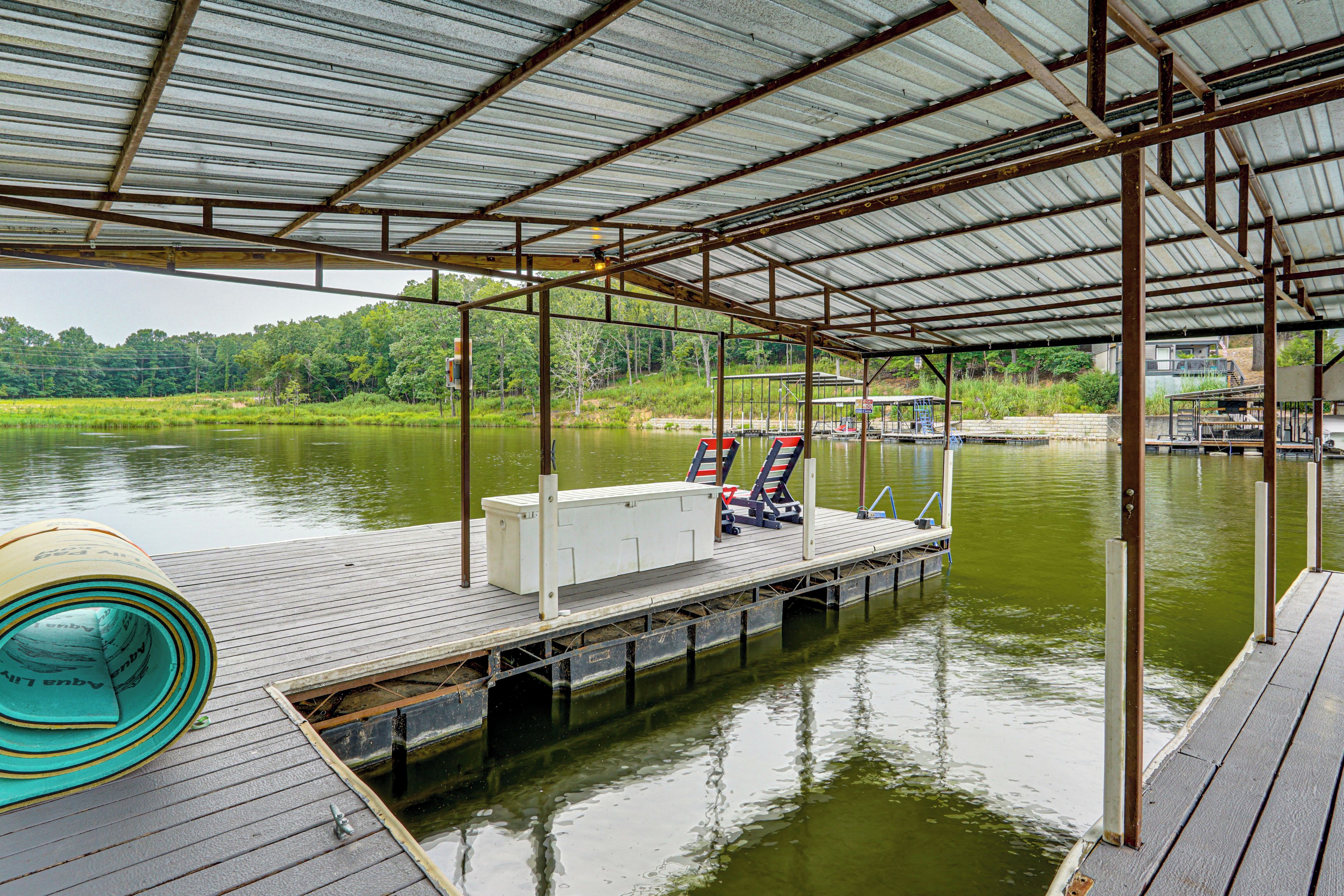 A covered dock with a metal roof, a boat, and a small building with a sign.