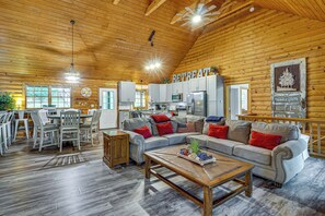 A log cabin interior with a dining area, a living room with a sofa and coffee table, and a kitchen with modern appliances. - Osage Beach Cabin With Private Dock and Lily Pad (Osage Beach)