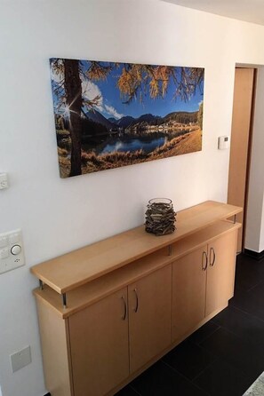 Une pièce avec un meuble en bois, un tableau représentant un paysage accroché au mur et une porte visible au fond.