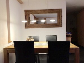 Un coin repas avec une table en bois, deux chaises, un miroir et un luminaire suspendu au plafond.
