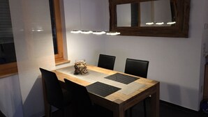 Ein Essbereich mit Holztisch, schwarzen Stühlen, einem zentralen Dekorationsobjekt und einer Wandleuchte.