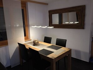 Ein Essbereich mit Holztisch, schwarzen Stühlen, einem zentralen Dekorationsobjekt und einer Wandleuchte.