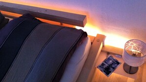 Ein Bett mit Kopfteil, ein Nachttisch mit Lampe und ein kleiner Bilderrahmen.