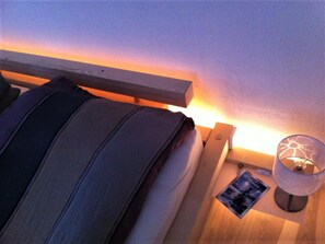 Ein Bett mit Kopfteil, ein Nachttisch mit Lampe und ein kleiner Bilderrahmen.