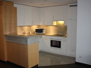 A modern kitchen with white cabinets, a microwave, an oven, and a granite countertop. - Weisshornblick, Sandhubel Appartement/Fewo, Bad, WC, Bergseite Appartement/Fewo by Interhome (Arosa)
