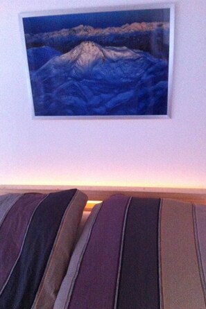 Une chambre avec un lit agrémenté d’oreillers à rayures, un tableau encadré représentant un paysage de montagne accroché au mur et une vue sur le ciel.