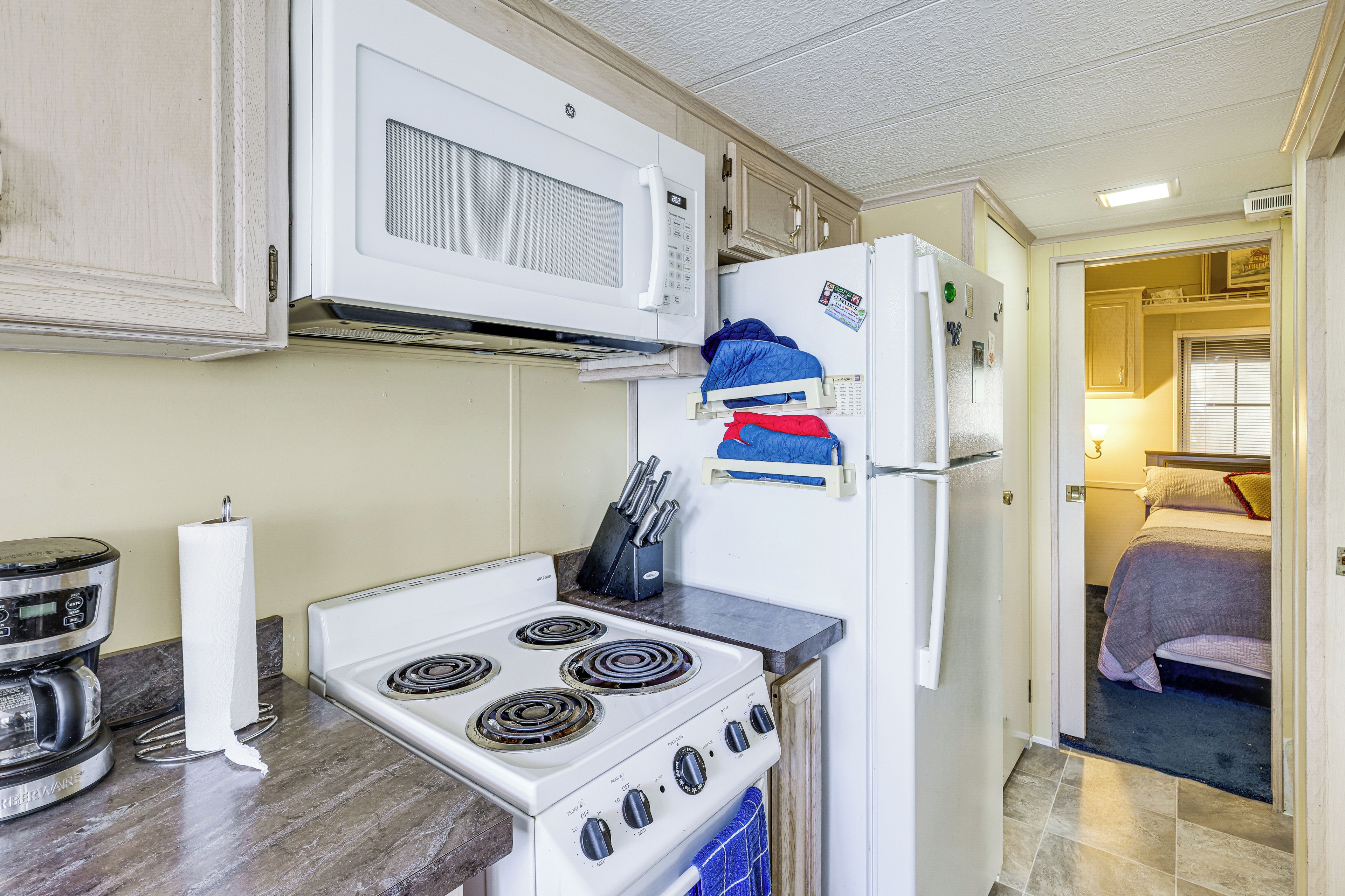 Une cuisine compacte équipée d’une cuisinière, d’un four à micro-ondes et d’un réfrigérateur, et une chambre à coucher visible à travers une porte ouverte.