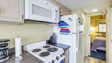Une cuisine compacte équipée d’une cuisinière, d’un four à micro-ondes et d’un réfrigérateur, et une chambre à coucher visible à travers une porte ouverte.