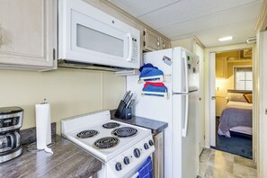 A compact kitchen with a stove, microwave, and refrigerator, and a bedroom visible through an open door.