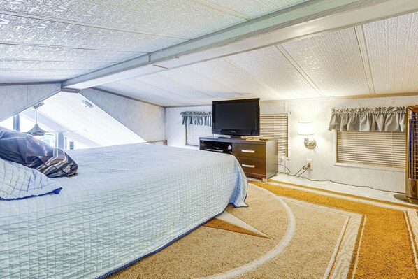 A bedroom with a bed, a television, a dresser, and a window with blinds.