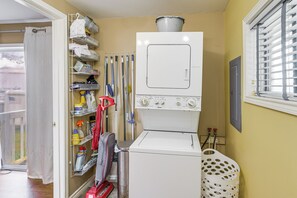 A laundry area with a washing machine, a drying rack, and shelves with cleaning supplies.