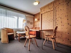 A hotel room with a wooden wardrobe, a dining table with chairs, a sofa, and a floor lamp. - Paradies 023 Appartement/Fewo,  , 2-Bettwohnung 2-Bettwohnung by Interhome (Arosa)