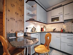 A modern kitchen with a wooden accent wall, a round dining table, and a built-in microwave. - Paradies 023 Appartement/Fewo,  , 2-Bettwohnung 2-Bettwohnung by Interhome (Arosa)