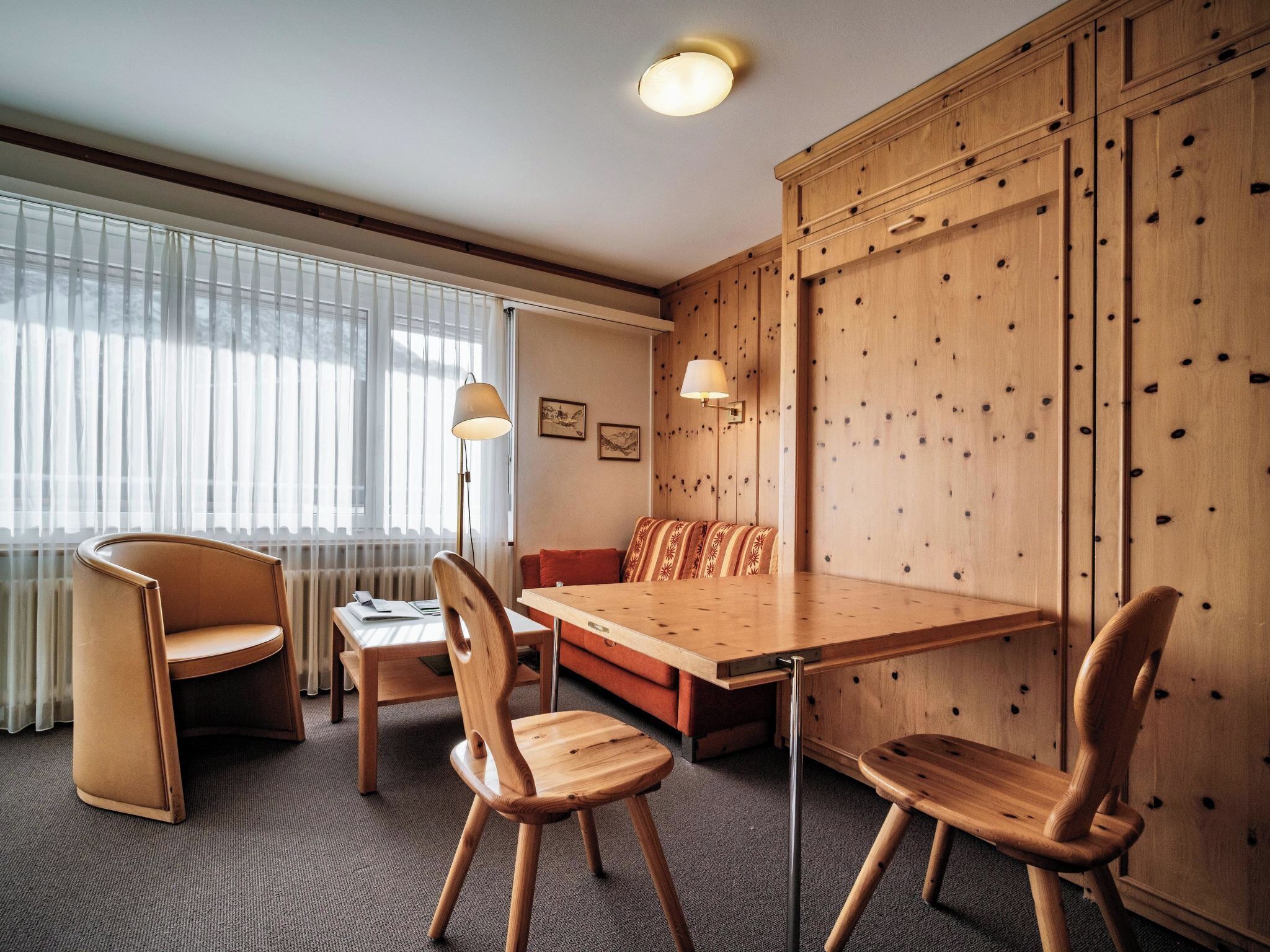 A hotel room with a wooden dining table, two chairs, a sofa, and a cabinet.