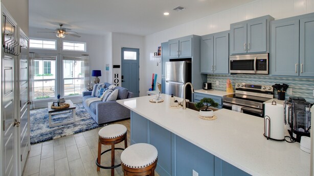 A modern kitchen with blue cabinets, a large island, stainless steel appliances, and a cozy living area with a sofa and coffee table. - Walk to Beach! North Padre Home w/ Pool Access (Corpus Christi)