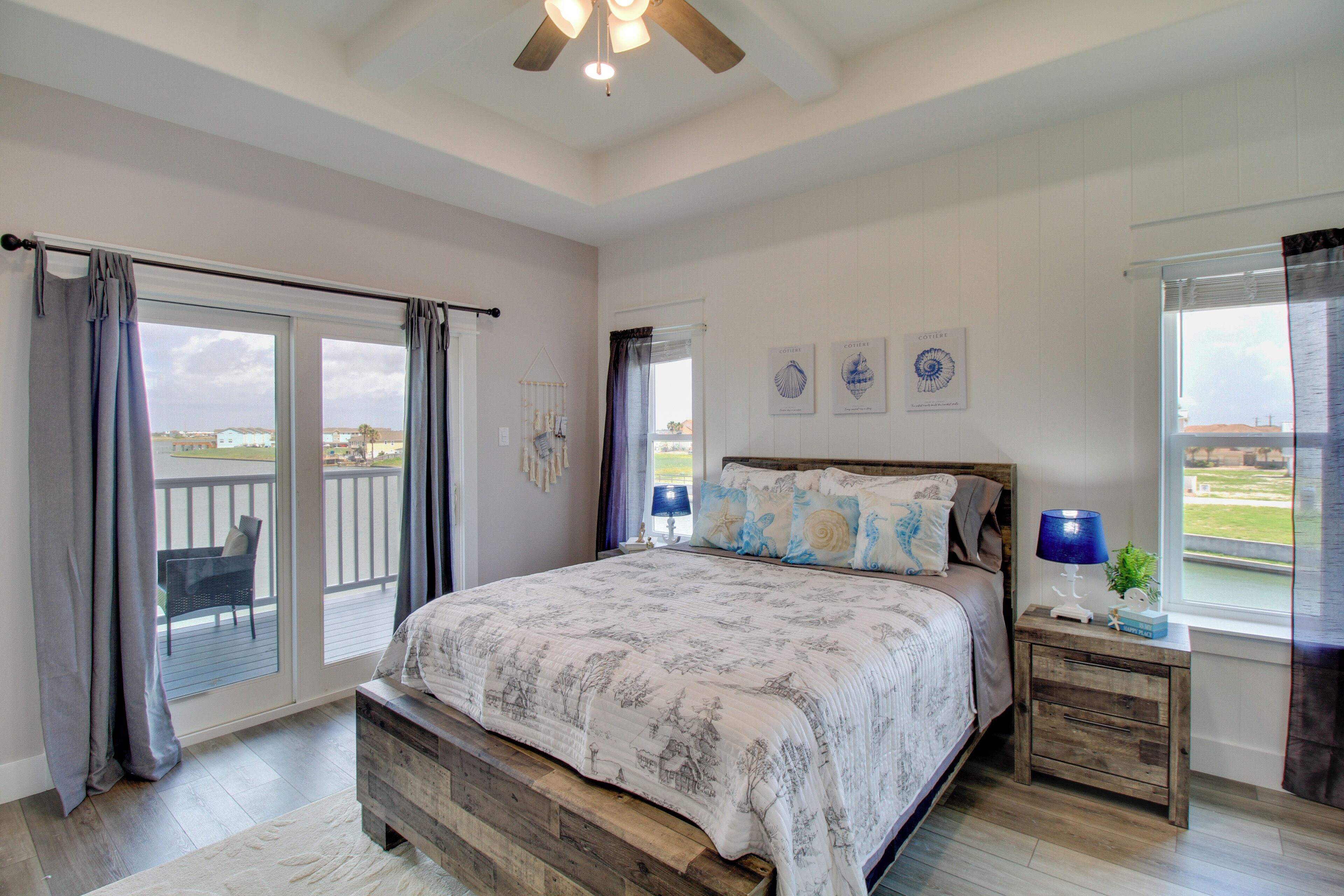 A bedroom with a large bed, a wooden nightstand, a window with curtains, and a view of the outdoors.