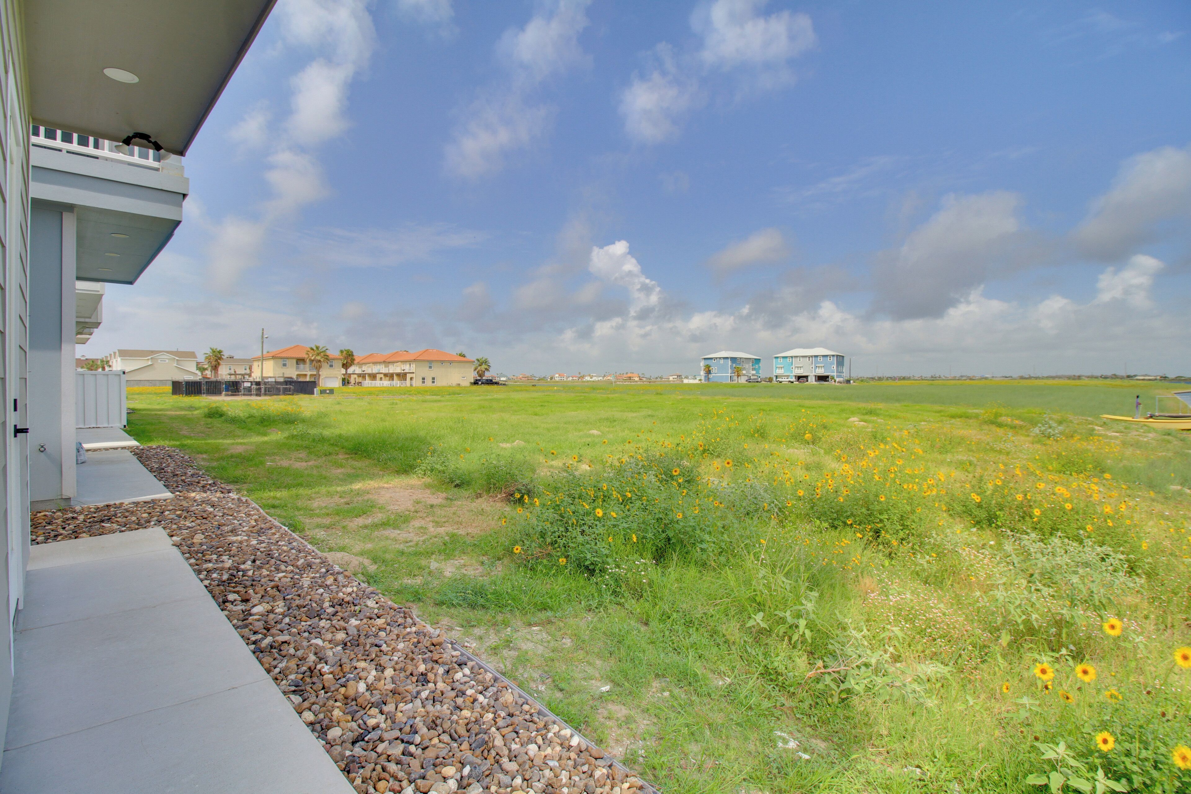 A residential area with a house, a grassy field with yellow flowers, and a clear sky.