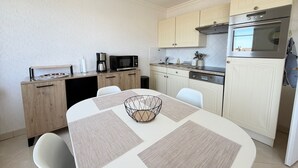 Una cucina compatta con tavolo, sedie, macchina del caffè, forno a microonde e forno integrato.