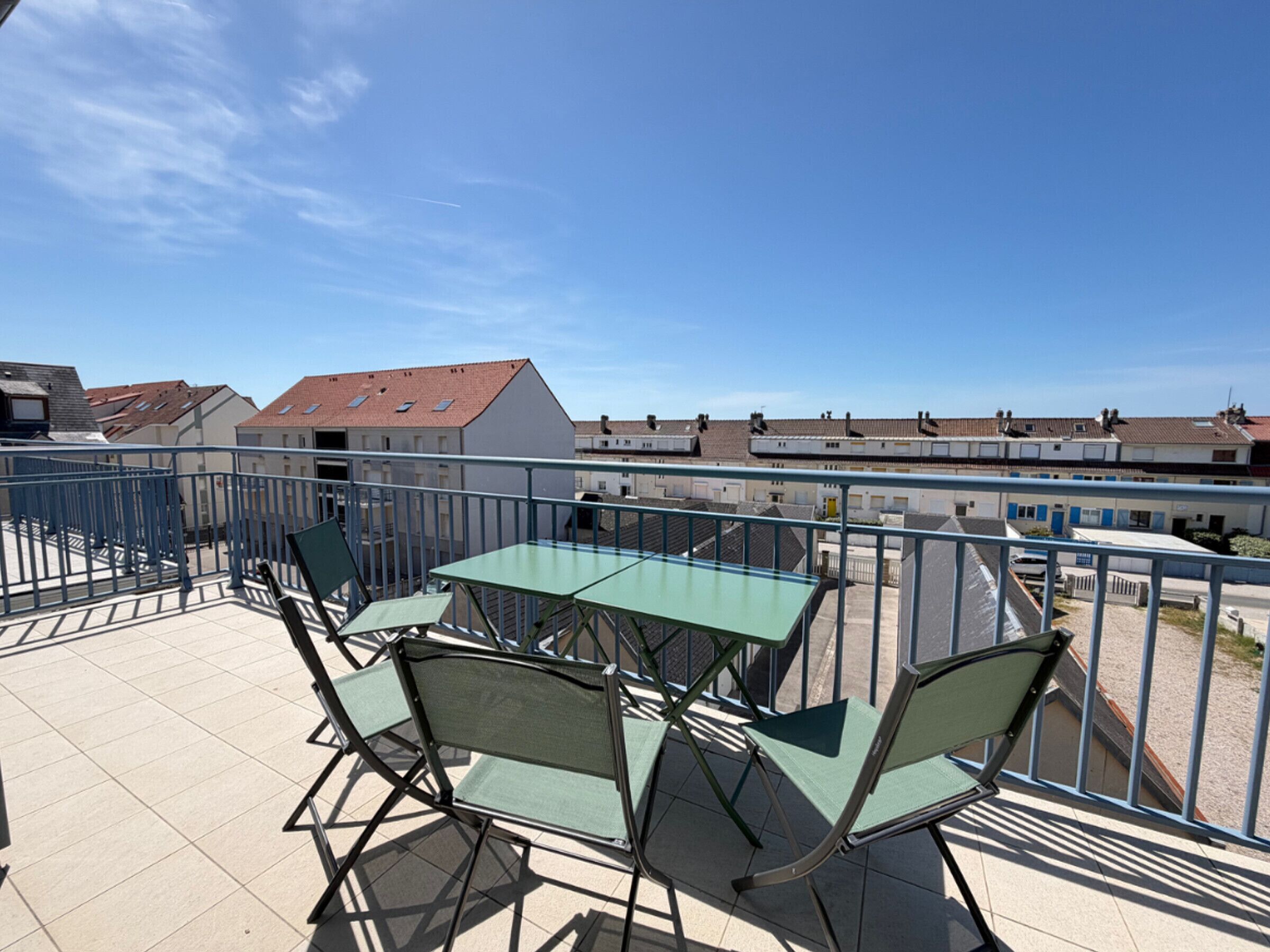 Ein Balkon mit Tisch und Stühlen, der auf einen Wohnbereich mit Häusern und bewölktem Himmel blickt.