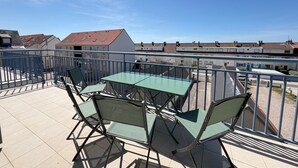 Un balcone con tavolo e sedie, affacciato su una zona residenziale con case e cielo sereno.