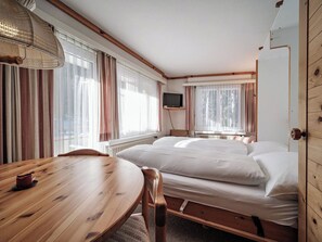 Een kamer met een houten tafel, twee bedden, een televisie en grote ramen voorzien van gordijnen.