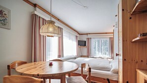 Una camera accogliente con un tavolo da pranzo in legno, sedie, un letto, una televisione e una finestra con tende.