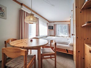 A cozy room with a wooden dining table, chairs, a bed, a television, and a window with curtains. - Paradies 203 Appartement/Fewo,  , 3-Bettwohnung 3-Bettwohnung by Interhome (Arosa)