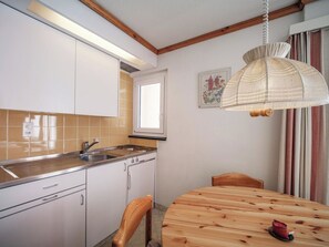 A kitchen with white cabinets, a sink, a window, and a wooden dining table with chairs. - Paradies 203 Appartement/Fewo,  , 3-Bettwohnung 3-Bettwohnung by Interhome (Arosa)