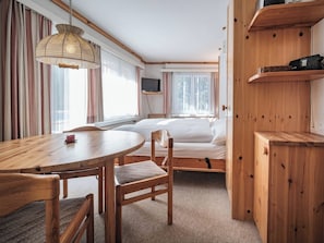 A hotel room with a wooden table, a bed, a TV mounted on the wall, and a window with curtains. - Paradies 203 Appartement/Fewo, Dusche, WC, 3-Bettwohnung 3-Bettwohnung by Interhome (Arosa)