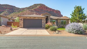 Ein zweistöckiges Haus mit Garage, umgeben von einem angelegten Garten mit verschiedenen Pflanzen und einem Berg im Hintergrund.