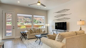 Ein Wohnzimmer mit einer Couch, Couchtisch, Fernseher und Wandkunst mit Blättern.