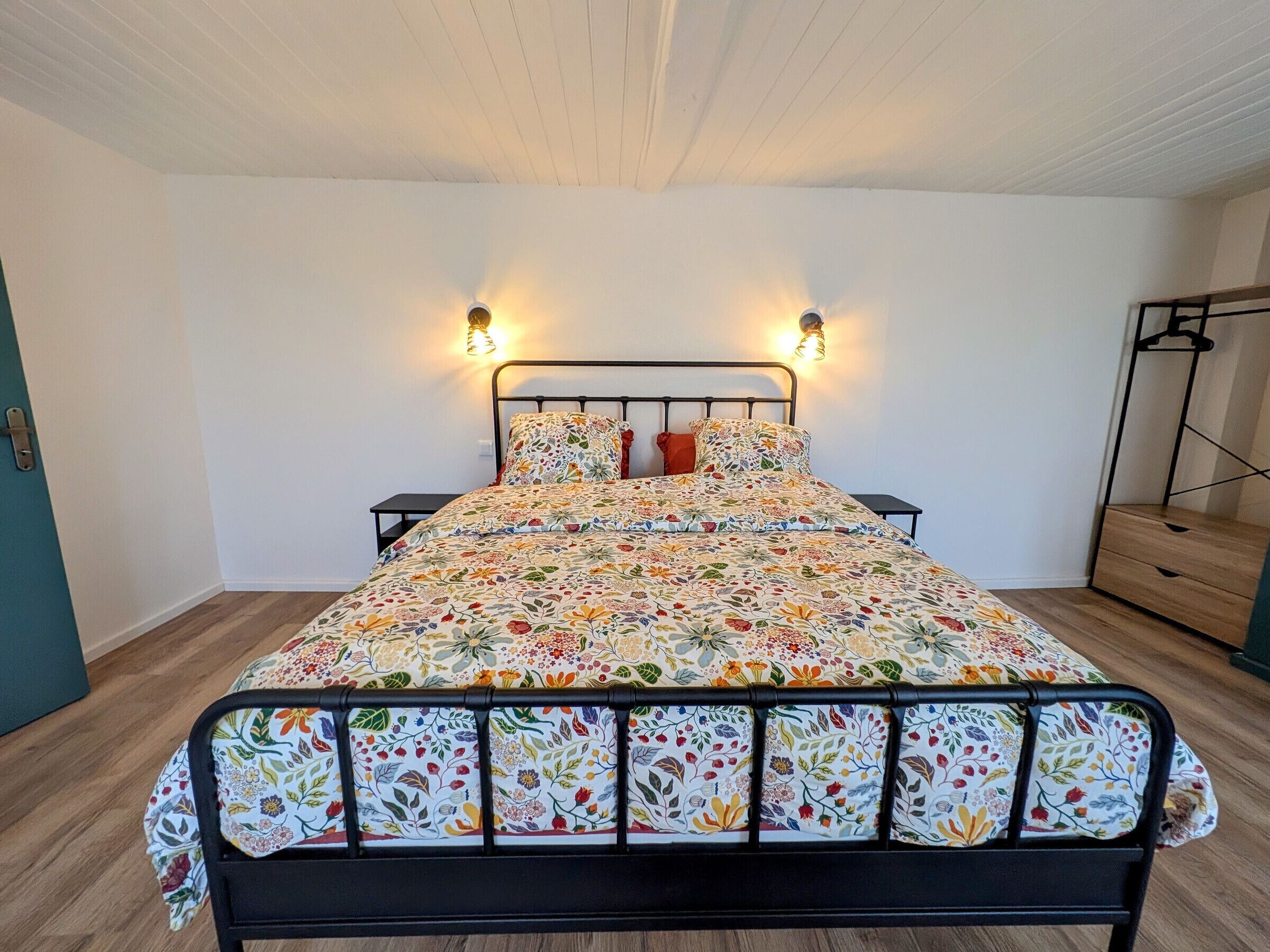 A bed with a floral bedspread, two bedside tables, and wall-mounted lights.